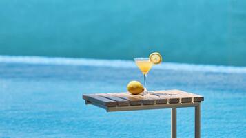 A poolside bar with a glass of cocktail and a lemon slice, overlooking a clear blue pool and a distant island.