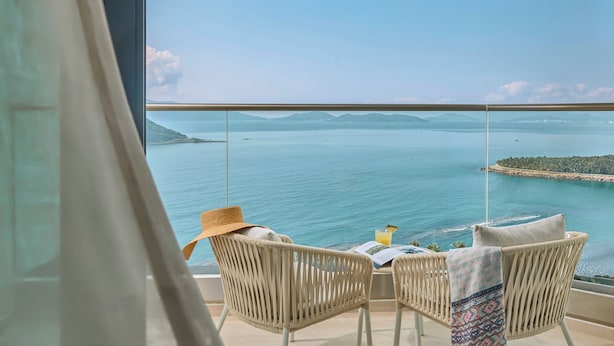 Un balcon avec des fauteuils en osier, une table et une vue sur la mer et le paysage lointain.