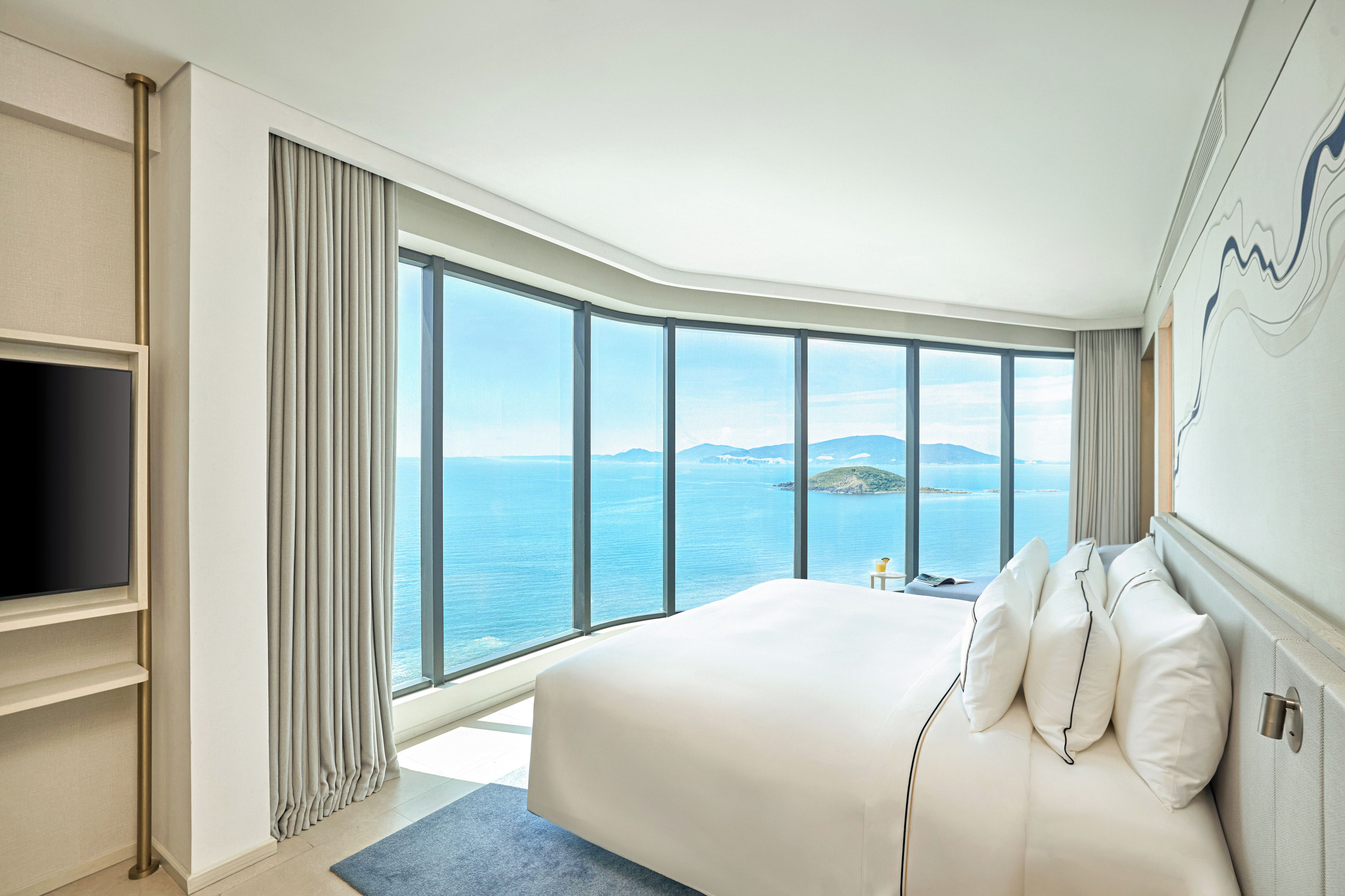 Una habitación de hotel moderna con una cama grande, un televisor de pantalla plana y vista al mar.