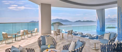 A rooftop lounge with outdoor seating, a pool, and a view of the sea and mountains.