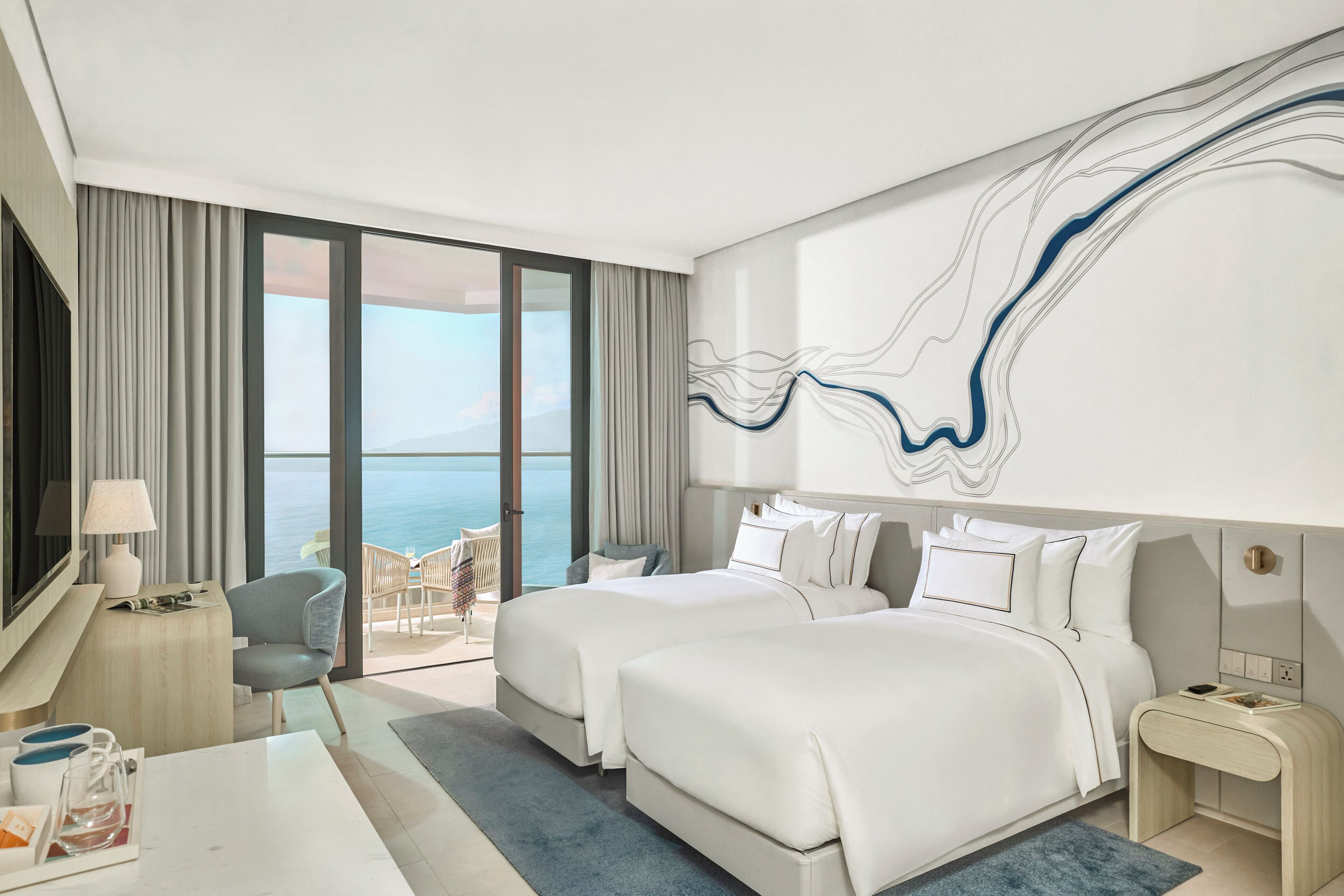 Une chambre d’hôtel avec deux lits, un bureau, une chaise, une télévision et une grande fenêtre donnant sur la mer.