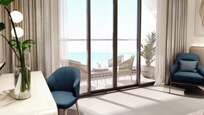 Un salon moderne doté d’une grande porte-fenêtre coulissante donnant sur un balcon avec vue sur la mer. On y trouve une table blanche ornée d’un vase contenant des plantes vertes, un fauteuil bleu et un canapé bleu avec un coussin.