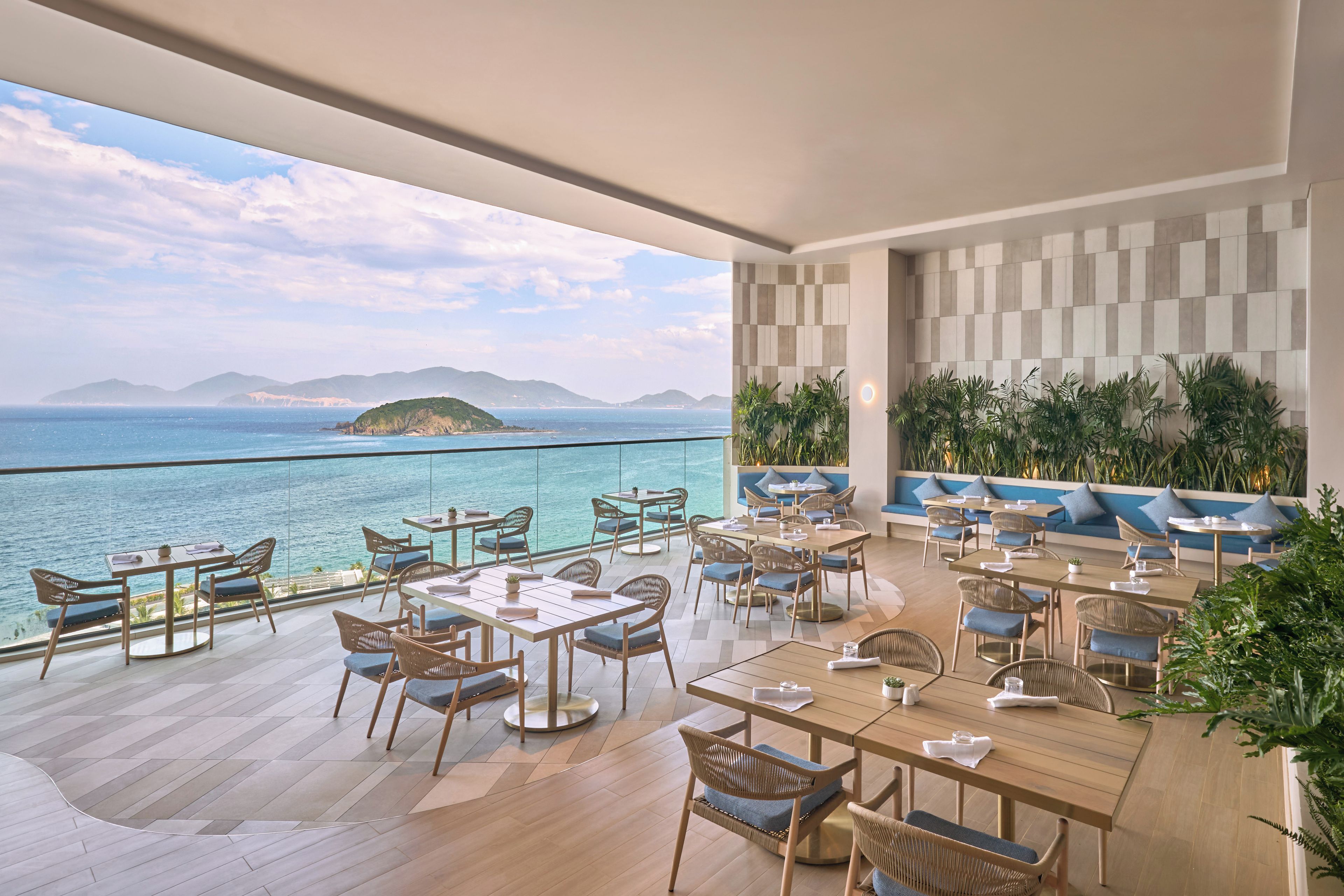 A spacious outdoor dining area with tables and chairs, overlooking a body of water and distant land.