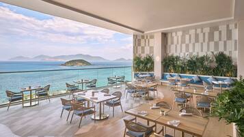 A spacious outdoor dining area with tables and chairs, overlooking a body of water and distant land.