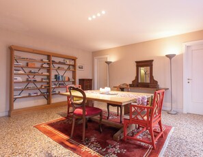 A dining area with a table, chairs, a bookshelf, a mirror, and a floor lamp. - Foscolo Apartments (Venice)
