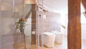 Une salle de bain moderne avec une douche à parois de verre, un plafond avec poutres apparentes et une baignoire blanche.