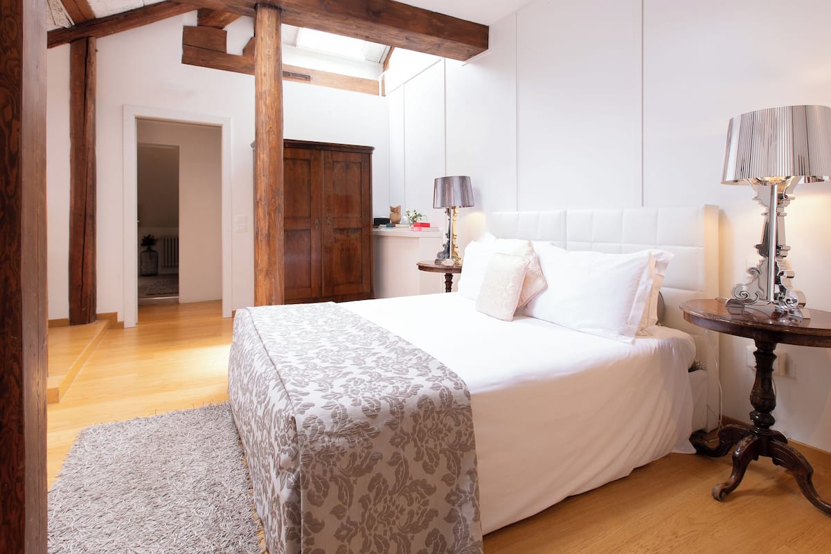 A bedroom with a bed, wooden beams, a nightstand, and a lamp.
