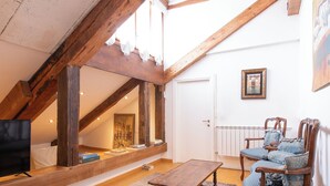 Une pièce de style « loft » avec des poutres en bois apparentes, une table en bois, deux fauteuils rembourrés, un téléviseur et un tableau encadré au mur.