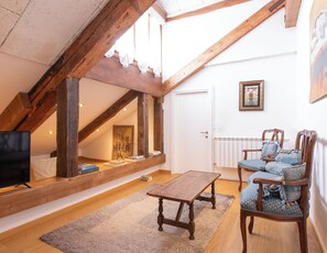 A loft-style room with exposed wooden beams, a wooden table, two upholstered chairs, a television, and a framed picture on the wall. - Foscolo Apartments (Venice)