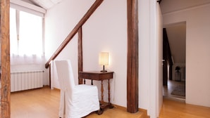 Une pièce avec une chaise en bois, une petite table avec une lampe et un radiateur.