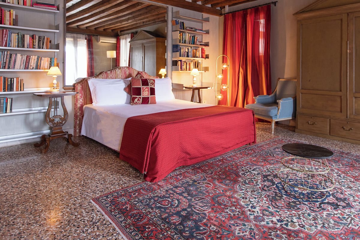 A bedroom with a large bed, bookshelves, a red carpet, and a wooden ceiling.
