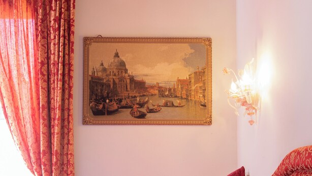 Une chambre avec un lit, des oreillers rouges, un tableau encadré représentant un paysage urbain et une fenêtre avec des rideaux rouges.