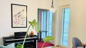 Ein modernes Wohnzimmer mit einem Klavier, einer großen Pflanze und einem gerahmten Kunstwerk an der Wand.