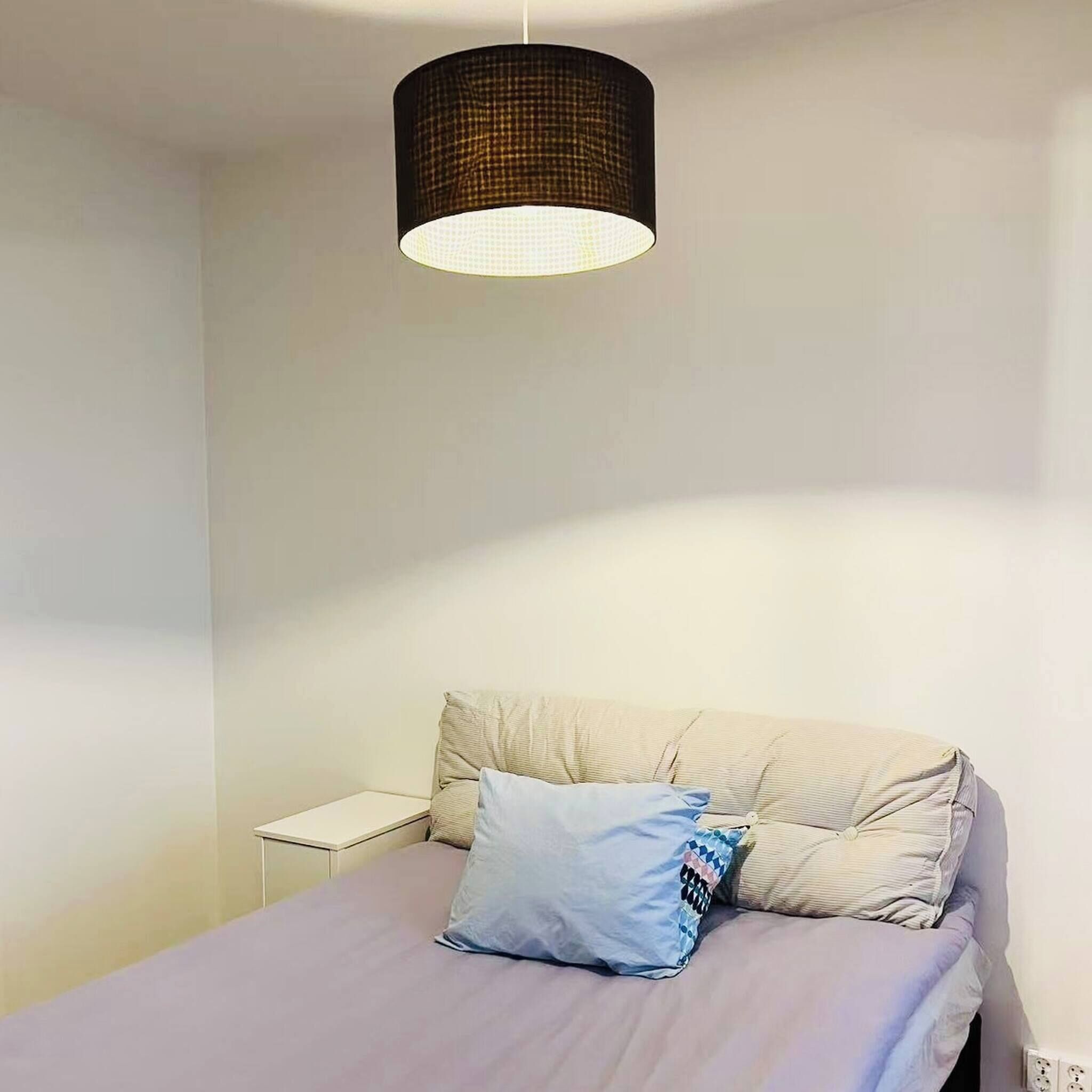 Een slaapkamer met een bed, een nachtkastje en een hanglamp.
