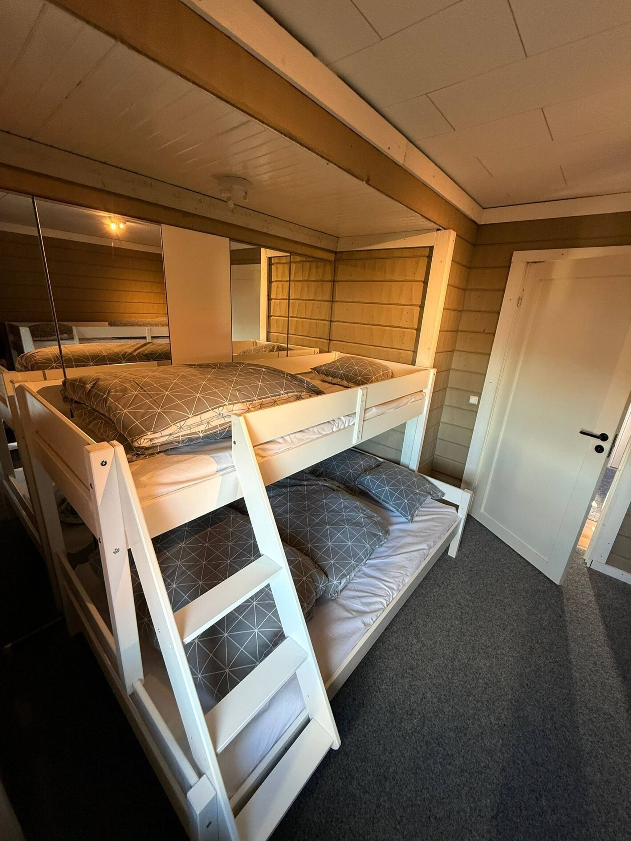 Habitación con literas, una escalera, una puerta y un espejo en la pared.