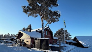 Un paisaje cubierto de nieve con una cabaña roja y un árbol grande.