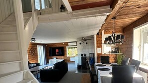 Amplia sala de estar con una escalera, una mesa de comedor para cuatro comensales y una cocina al fondo.