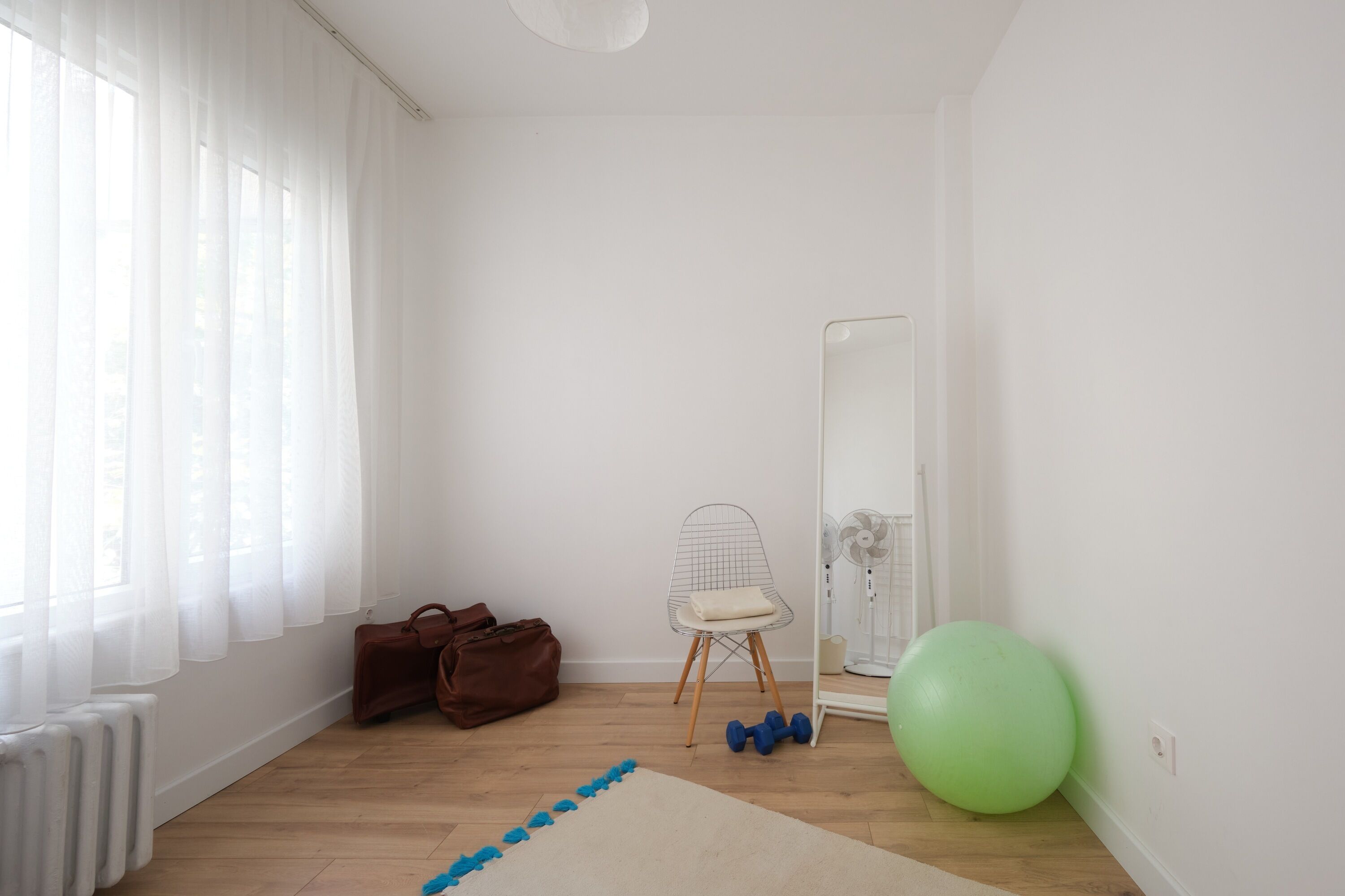 Um quarto com um radiador, uma cadeira, uma bola de exercício verde e um par de halteres.