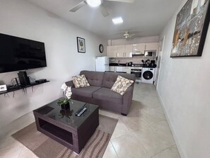 Ein Wohnzimmer mit einer Couch, einem Couchtisch, einem Fernseher und einer Küche im Hintergrund.