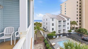 A balcony with white chairs, a pool area, and a view of a multi-story building with balconies. - Tropical Tide Large Group Beach Retreat Sleeps 24 (North Myrtle Beach)