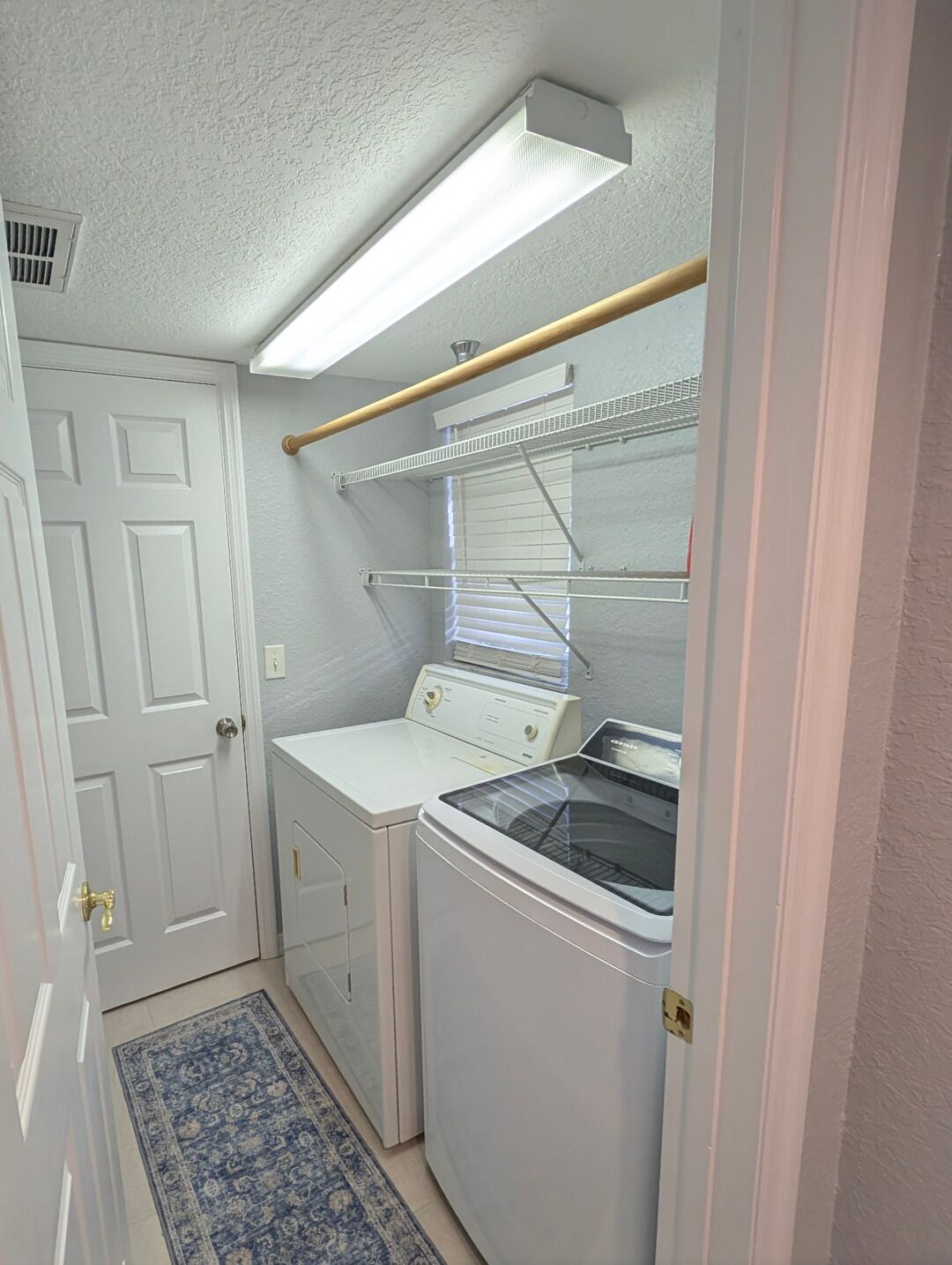 A compact laundry room with a washing machine, dryer, and a drying rack.