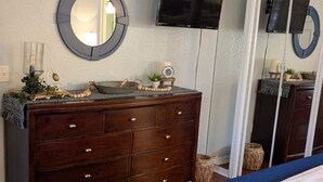 Camera da letto con un letto grande, una cassettiera, uno specchio rotondo, una TV a schermo piatto montata a parete e un grande specchio nell'armadio.