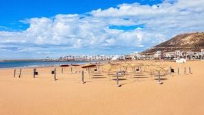 A beach with sun loungers and umbrellas, a clear sky, and buildings in the background. - Apartment agadir bay flat luxe (Agadir)
