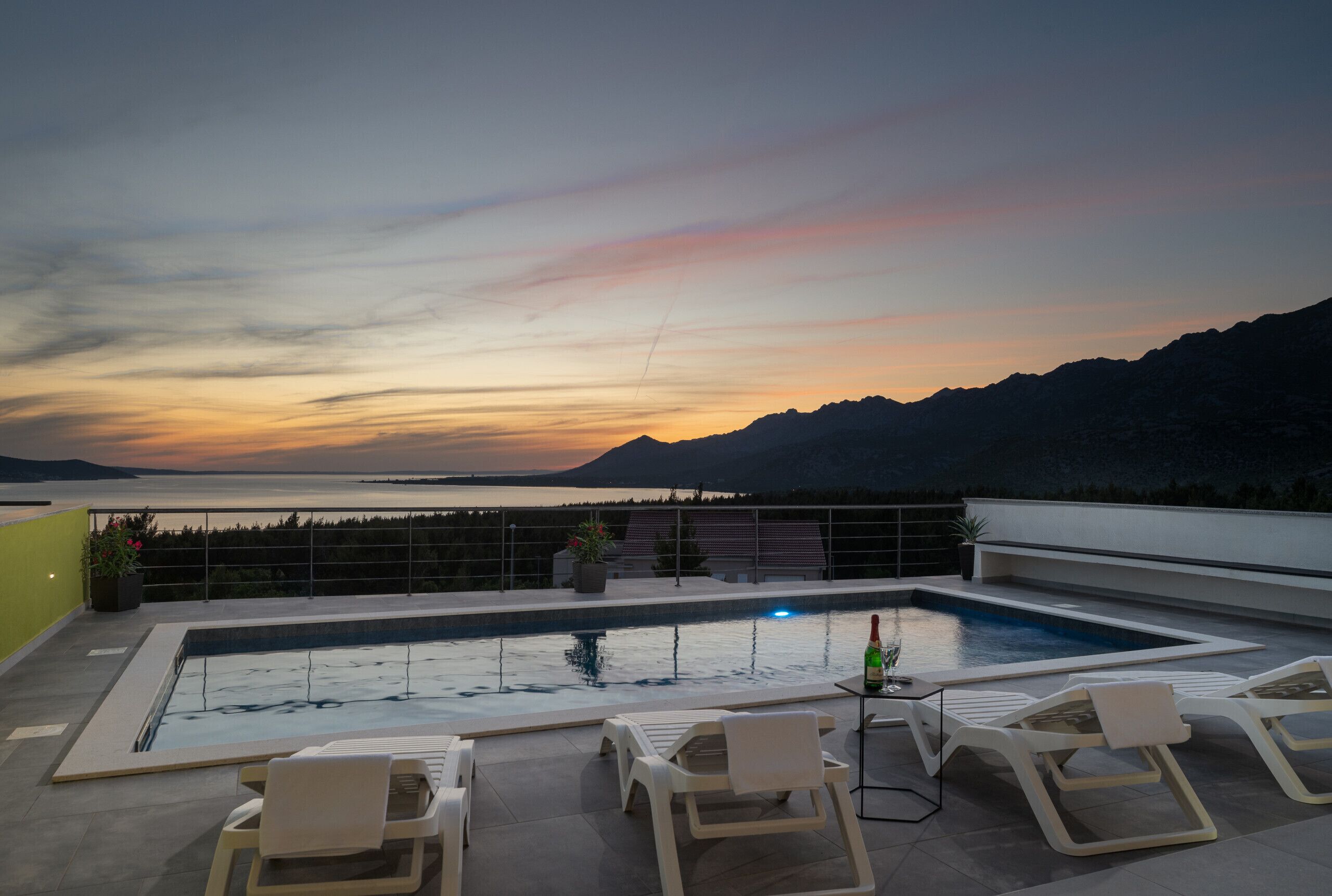A rooftop pool with lounge chairs, a table, and a bottle of champagne.