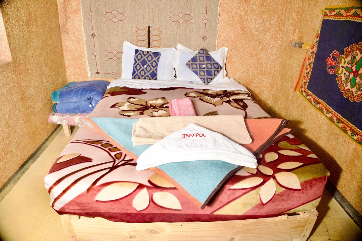 A bed with patterned bedding and pillows, a wooden headboard, and a decorative wall hanging.