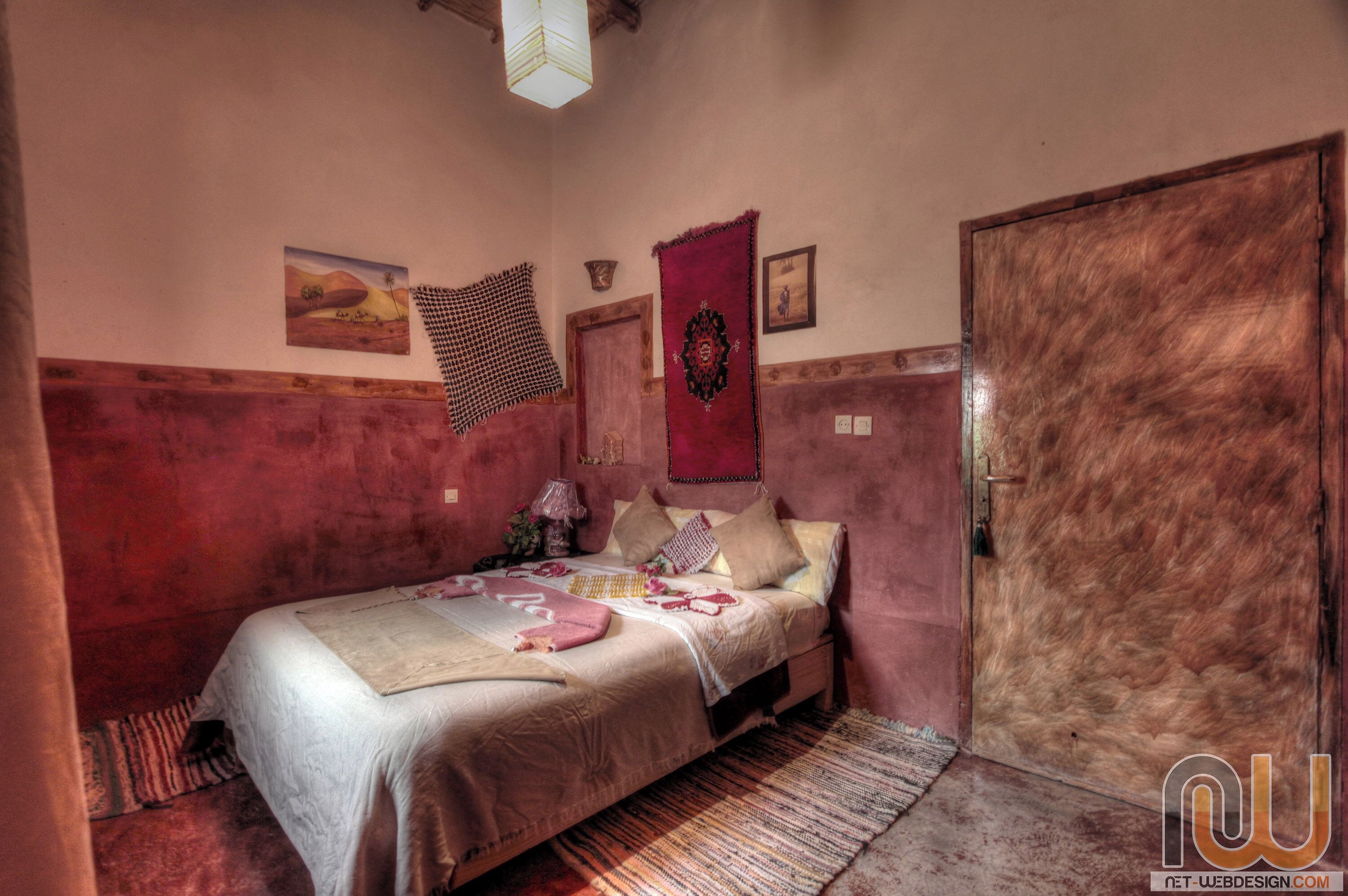 Une chambre à coucher avec un lit, une porte et un mur orné d’une tapisserie et d’un tableau.
