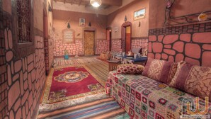 A cozy room with a stone wall, a wooden door, a patterned rug, and a bed with a colorful blanket. - Maison d'hôtes tifaoute ait Ben haddou  (Ait Benhaddou)