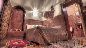 A traditional room with a bed, a wall-mounted light fixture, and a patterned rug. - Maison d'hôtes tifaoute ait Ben haddou  (Ait Benhaddou)