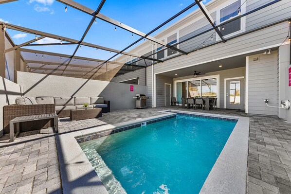 A covered outdoor swimming pool with a patio area, seating, and a covered walkway. - 16148 Palm Frond Avenue (Clermont)