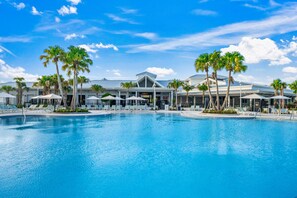 A large swimming pool surrounded by palm trees and lounge chairs, with a modern building in the background. - 16148 Palm Frond Avenue (Clermont)