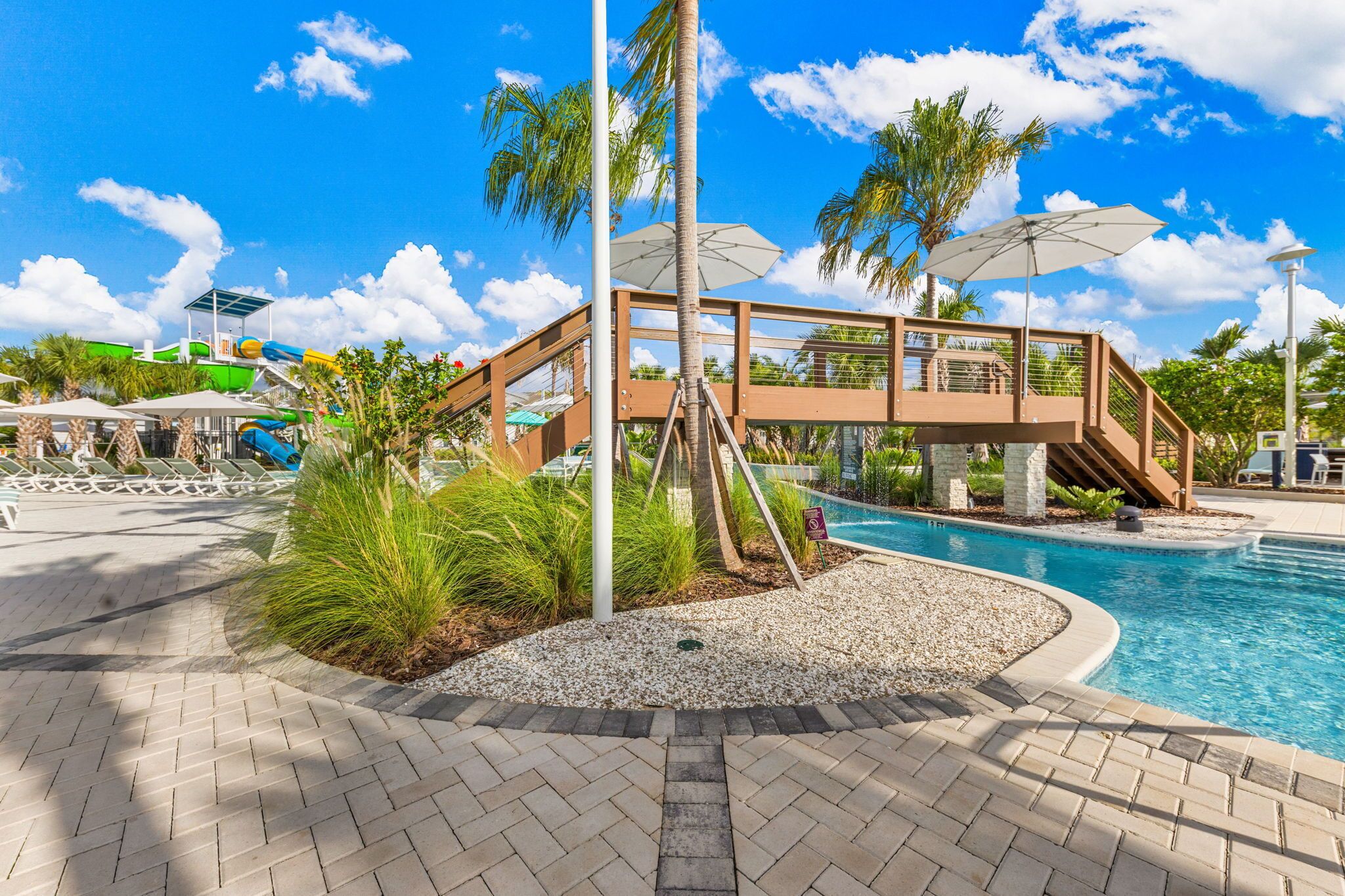 A pool area with a water slide, palm trees, and a covered seating area.