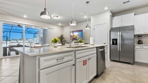 A modern kitchen with white cabinetry, stainless steel appliances, pendant lighting, and a large island with a sink. - 16148 Palm Frond Avenue (Clermont)