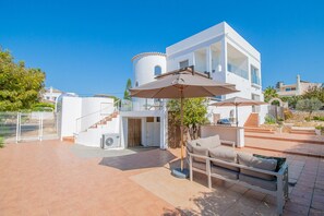 Eine moderne Villa mit geräumiger Terrasse, Sitzgelegenheiten im Freien und freiem Blick auf die umliegende Landschaft.