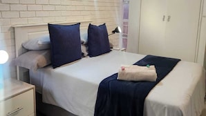 Una camera da letto moderna con parete in mattoni, un letto con biancheria blu scuro, un armadio bianco e una ventola a soffitto.