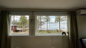 A room with two large windows offering views of a lake and trees. - Camp Caroli Family House (Jukkasjarvi)