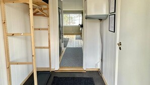 A hallway with a wooden shelf unit, a black carpet, and a white door with framed certificates. - Camp Caroli Family House (Jukkasjarvi)