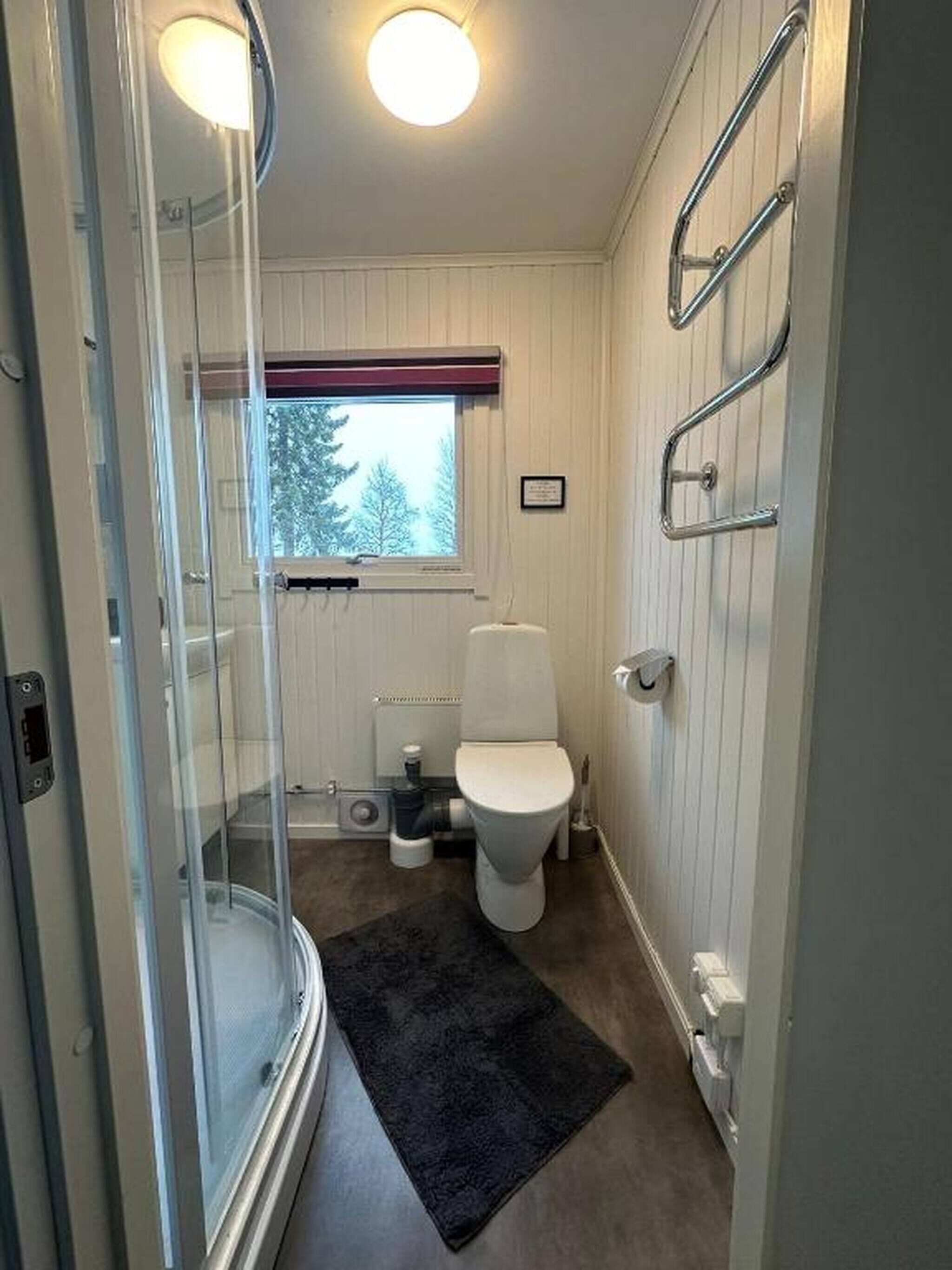 A compact bathroom with a glass shower enclosure, a toilet, and a radiator.