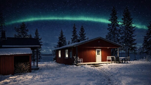 A cabin with a wooden exterior, a porch with chairs, and a snow-covered ground. - Camp Caroli Family House (Jukkasjarvi)