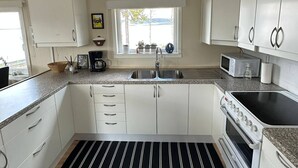 A kitchen with white cabinets, a black and white striped floor, a microwave, a stove, and a window with a view. - Camp Caroli Family House (Jukkasjarvi)