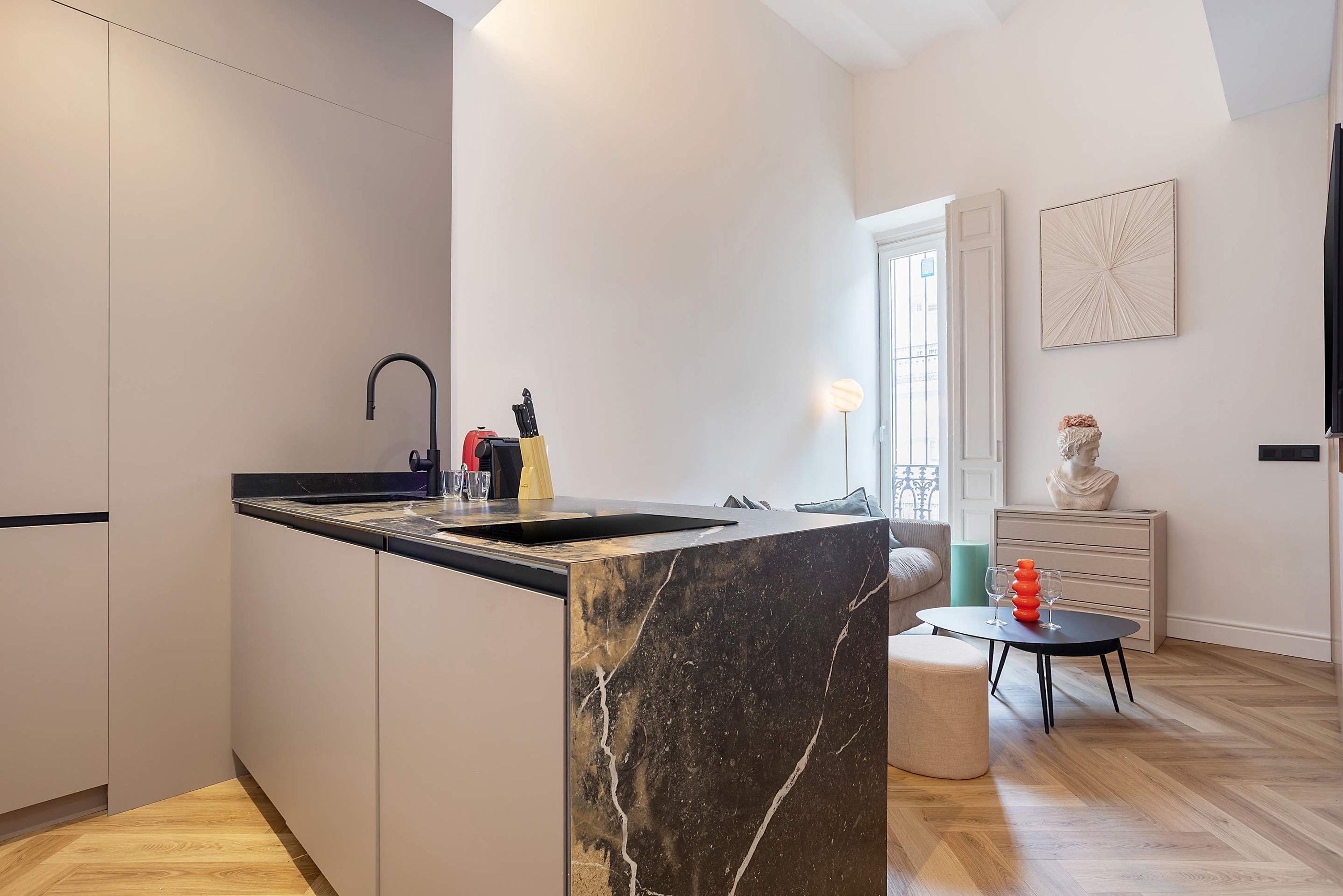 A modern kitchen with a marble island, a black faucet, and a dining area with a small table and chairs.