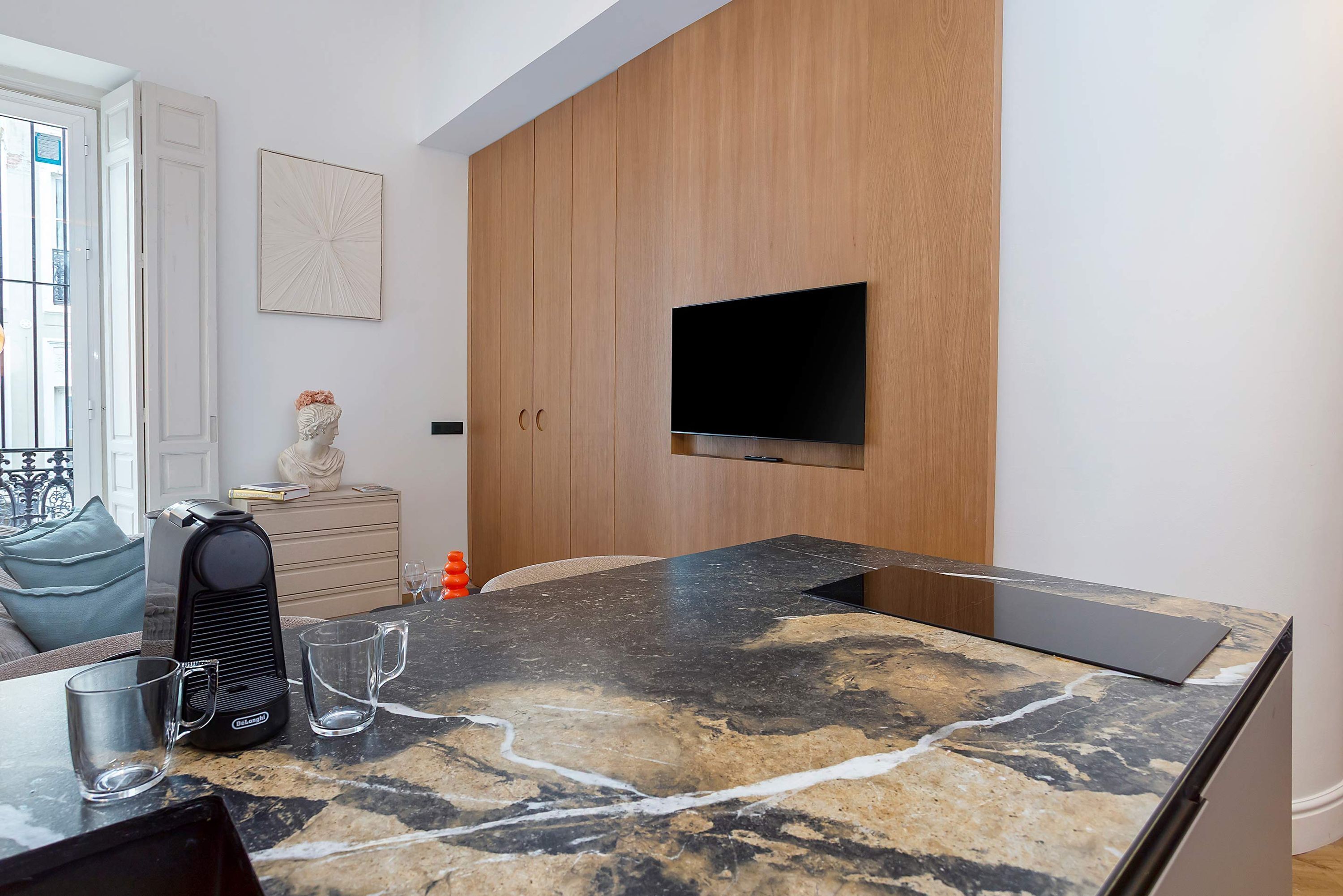 Eine moderne Küche mit Marmorarbeitsplatte, einer Kaffeemaschine und einem an der Wand befestigten Flachbildfernseher.