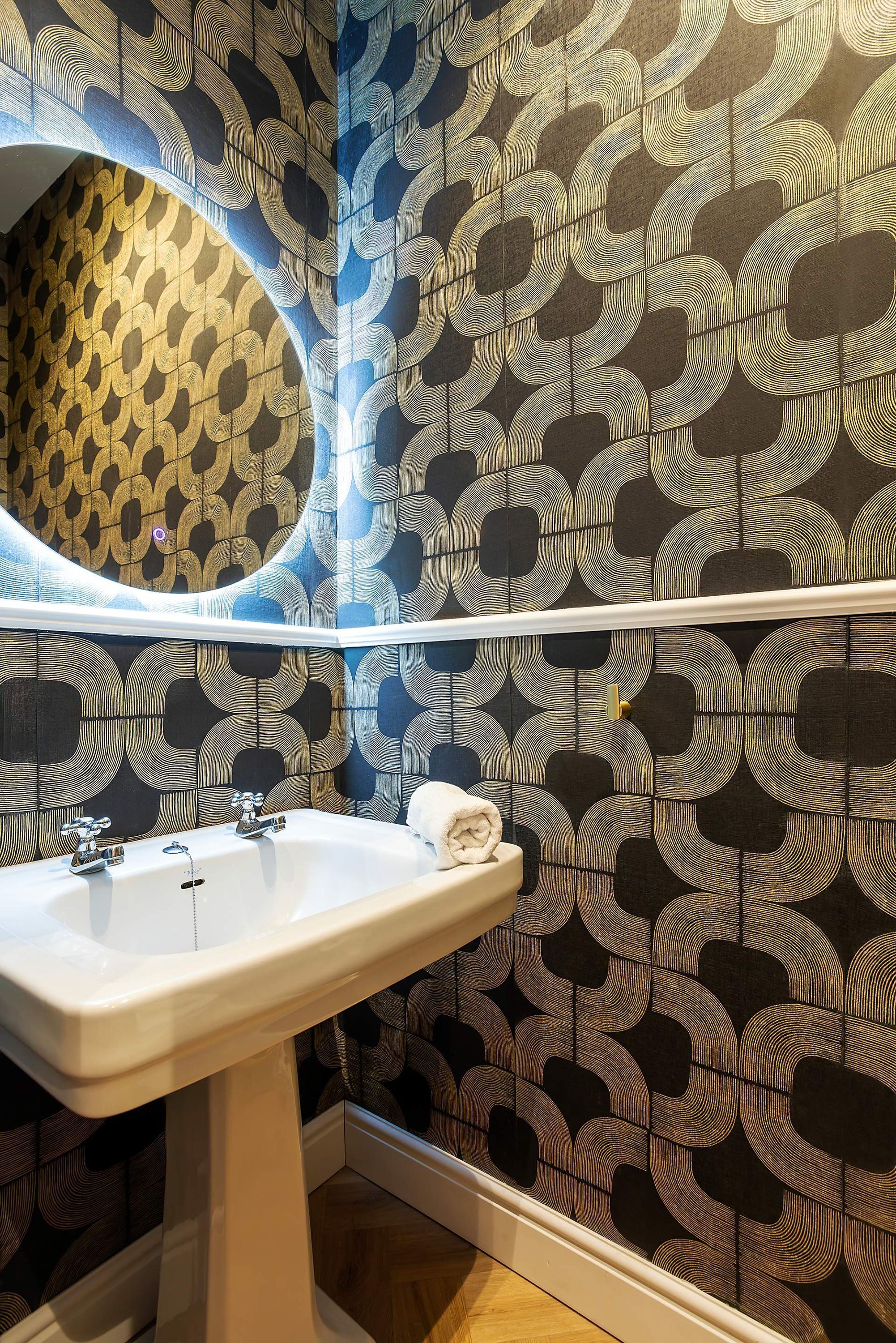 A bathroom with a white sink, a mirror, and patterned wallpaper.