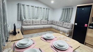 A dining area with a wooden table set for four, a grey sectional sofa, and a black refrigerator. - Parkdean Crimdon Heated Sea View Caravan (Hartlepool)