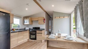 A compact kitchen with wooden cabinets, a microwave, a stove, and a dining area with a table set for two. - Parkdean Crimdon Heated Sea View Caravan (Hartlepool)