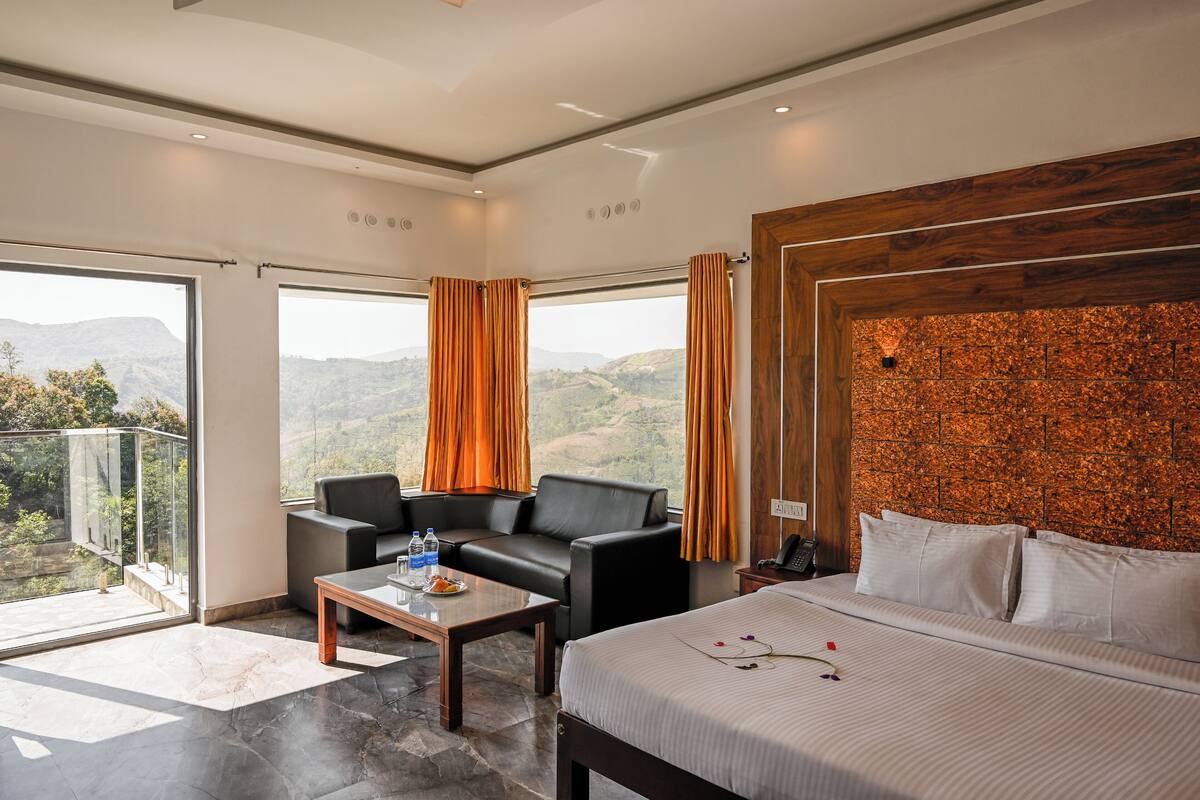 Una habitación de hotel moderna con una cama grande, un cabecero de madera, una zona de estar con una mesa y un balcón con vistas a la montaña.
