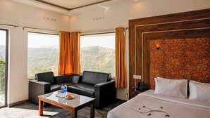 Habitación de hotel con cama, sofá, mesa de centro y vistas a las montañas.